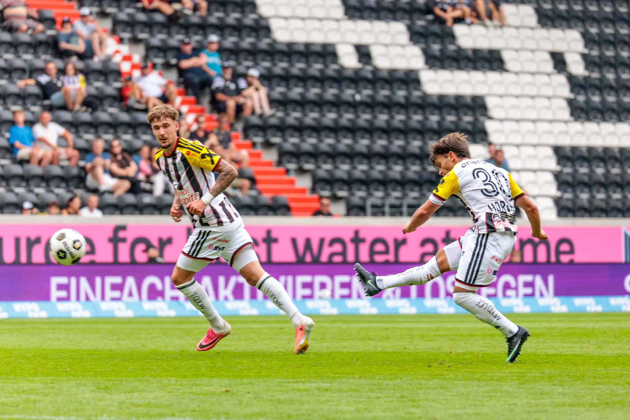 LASK-Spieler zieht aus der Distanz ab, leere Tribünen mit roter Treppe im Hintergrund, sichtbare Konzentration im Anlauf.