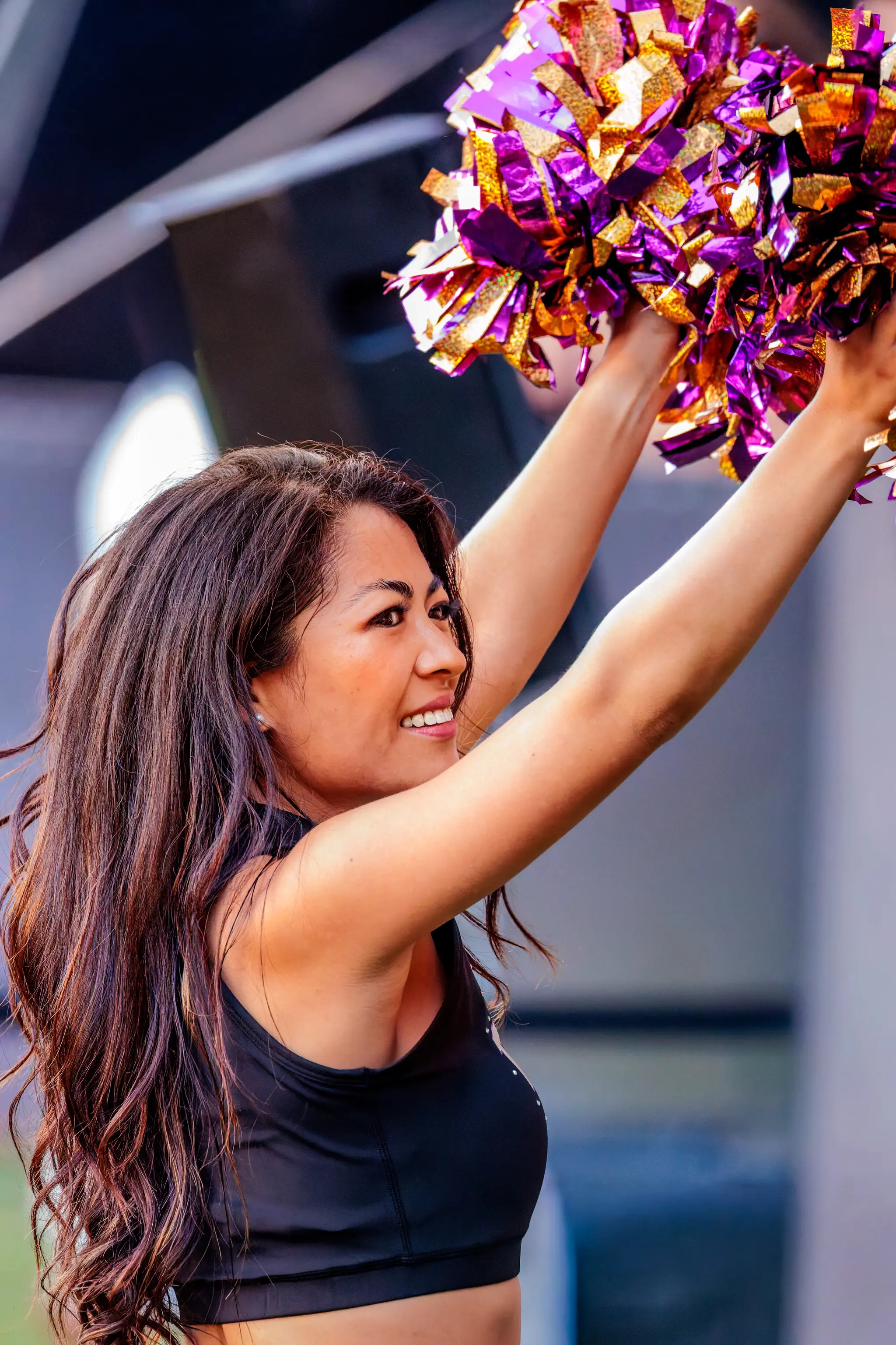 Portrait einer Tänzerin des Vienna Vikings Cheer Squads mit erhobenen lila-goldenen Pompons – am Spielfeldrand in einer Spielpause im zweiten Viertel.