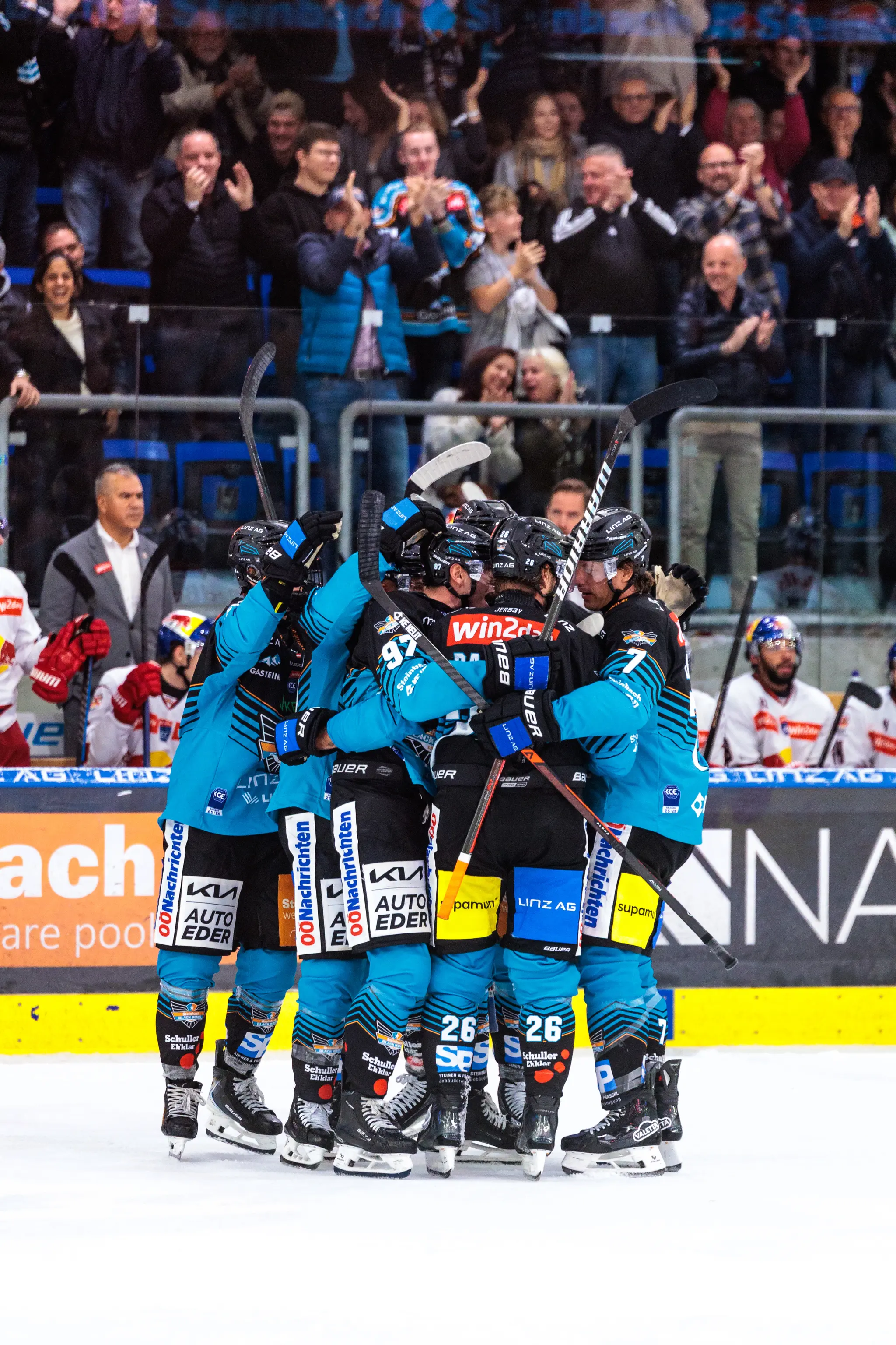 Die Eishockeyspieler der Steinbach Black Wings Linz feiern ihren Sieg mit einer emotionalen Jubeltraube auf dem Eis vor den applaudierenden Fans
