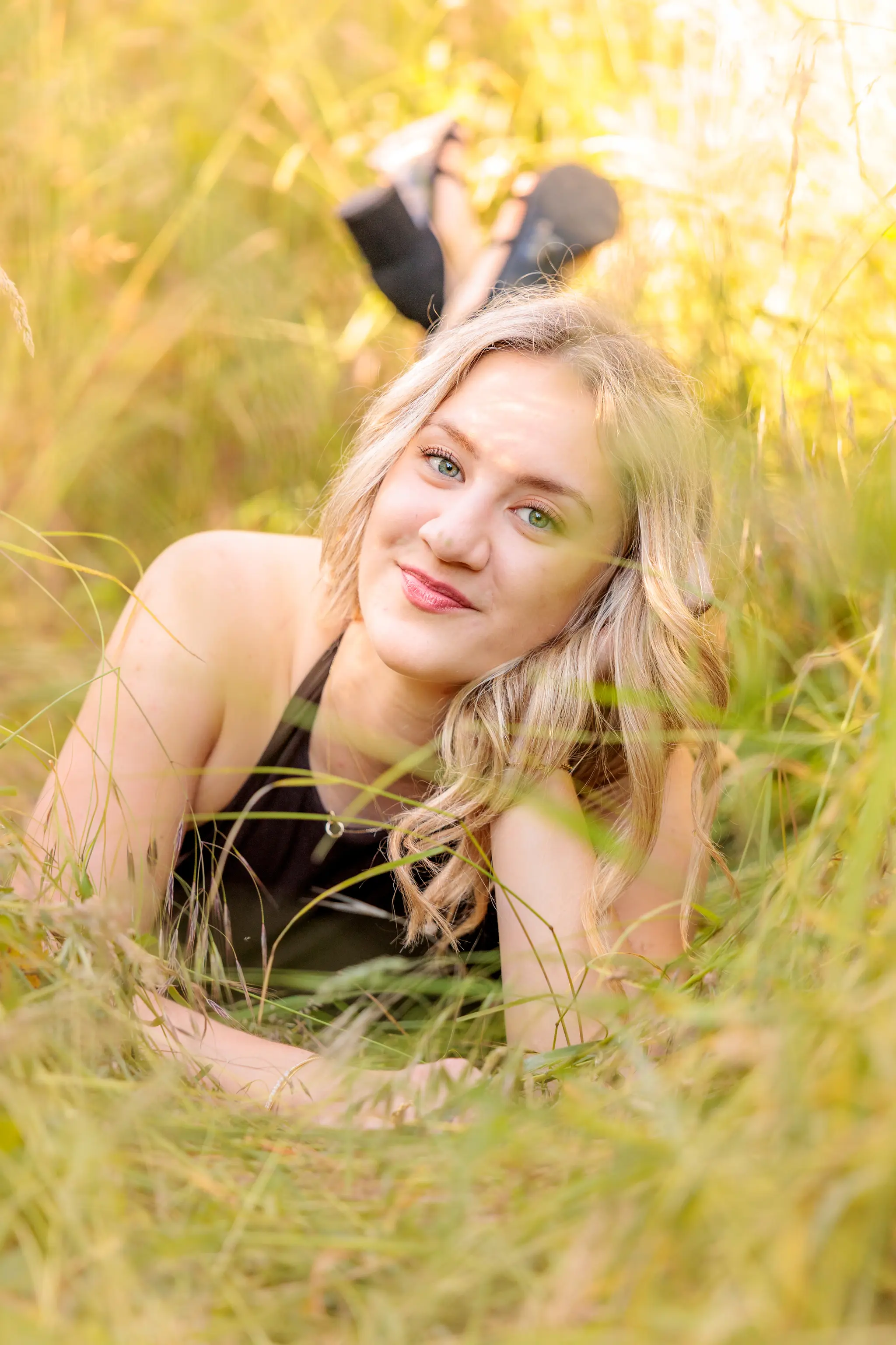 Ein Porträt einer jungen Frau mit blonden Haaren und grünen Augen, die entspannt in einer sonnigen Wiese liegt und lächelt 