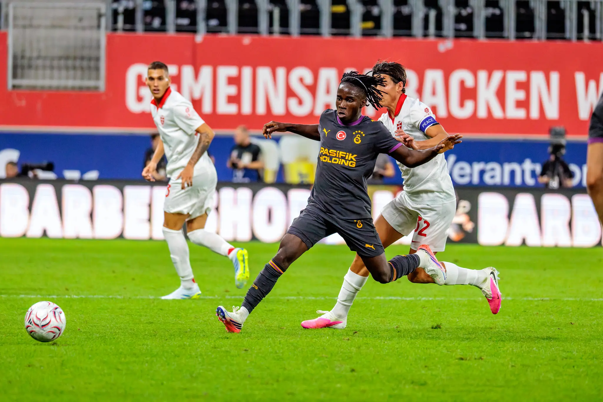 Galatasaray-Spieler mit Dreadlocks im Zweikampf mit Monza-Spieler Nummer 32, beide Arme im Kampf um Position.