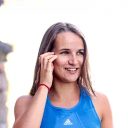 Eine lächelnde junge Frau mit braunen Haaren und blauen Augen trägt ein blaues Adidas-Sporttop und blickt vor hellem Hintergrund zur Seite lens: 56mm F1.4 DC DN | Contemporary 018