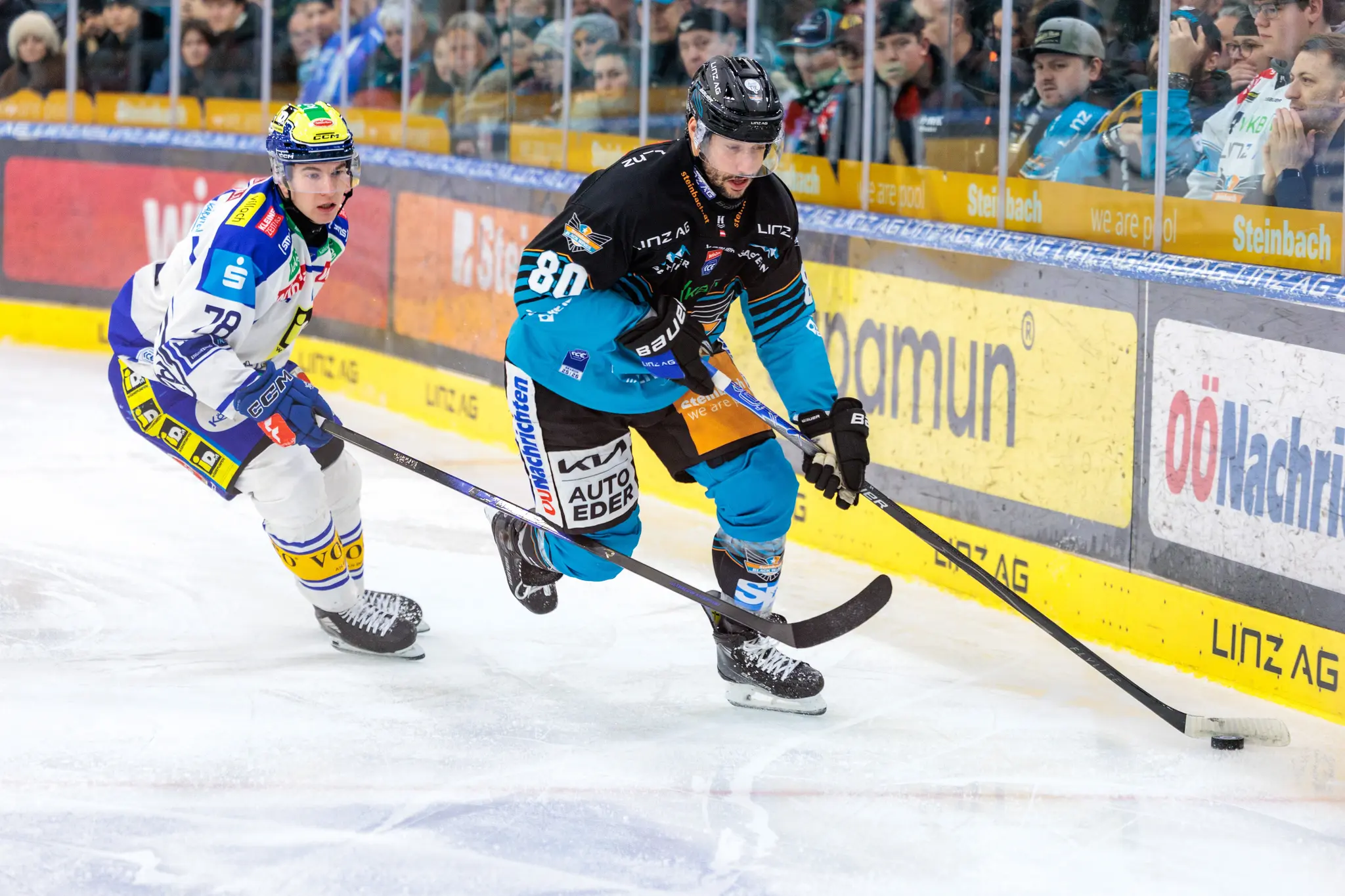 Ein Eishockeyspieler der Black Wings Linz mit der Nummer 80 dribbelt den Puck über das Eis, verfolgt von einem Gegenspieler des VSV