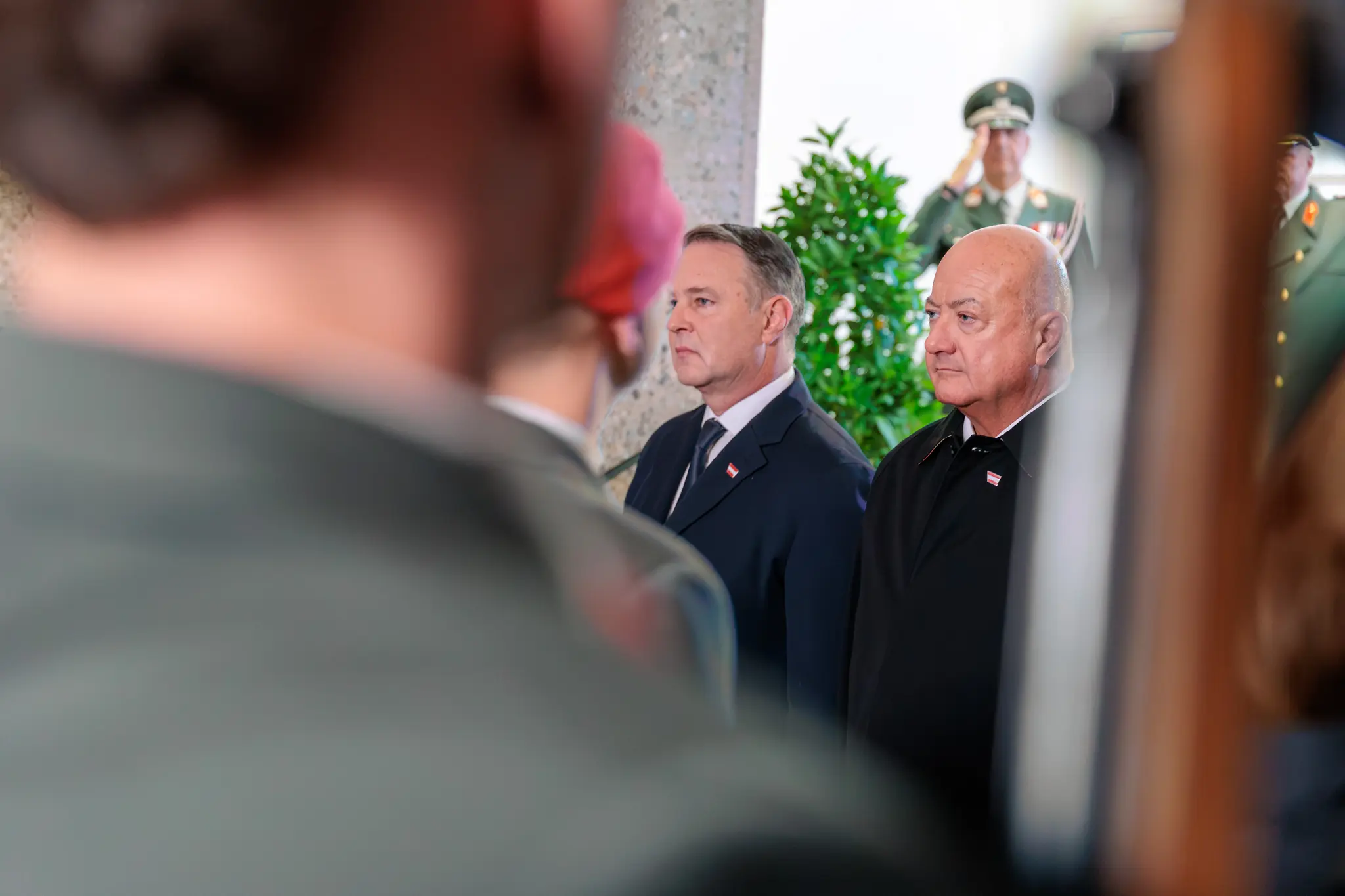Vizekanzler Andreas Babler und Bundeskanzler Christian Stocker stehen im Weiheraum des Äußeren Burgtors und verfolgen die Kranzniederlegung, hinter ihnen salutiert ein Gardesoldat.
