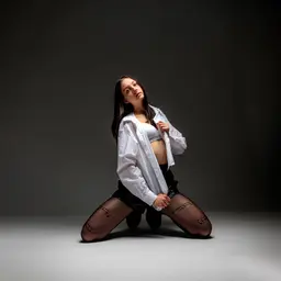 Eine junge Frau kniet in einem offenen weißen Hemd, einem weißen Sport-BH und schwarzen Strümpfen mit Schriftzug auf einem dunklen Studiohintergrundlens: RF50mm F1.8 STM
