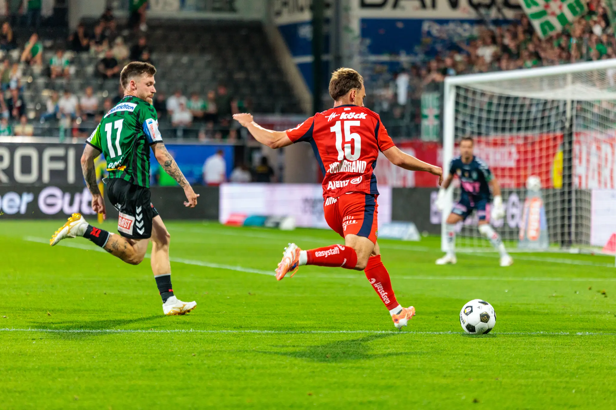 Ein Spieler von Rapid Wien führt einen Torschuss aus, während ein Spieler der SV Ried versucht, den Ball zu erreichen