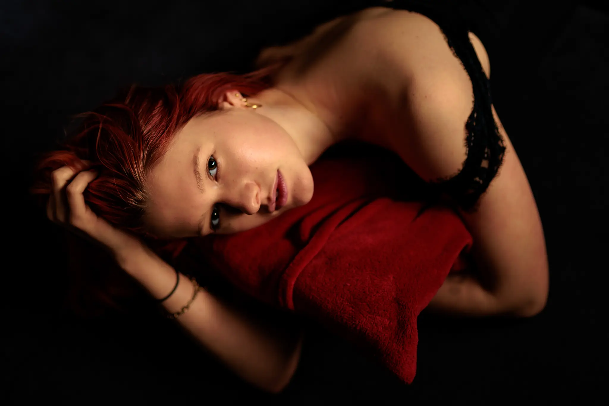 Ein stimmungsvolles Beauty-Portrait zeigt Sarah mit ihren roten Haaren, wie sie auf einem samtigen roten Kissen liegt und einen intensiven Blick in die Kamera wirft