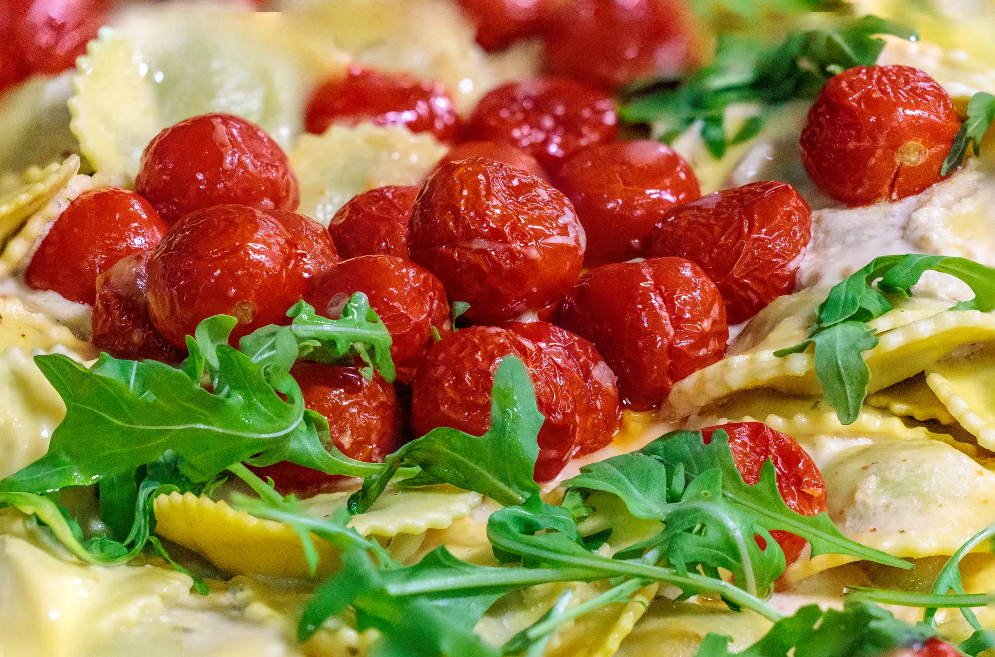 Nahaufnahme eines Pastagerichts mit frischen Ravioli in einer cremigen Soße, garniert mit gerösteten Kirschtomaten und Rucola