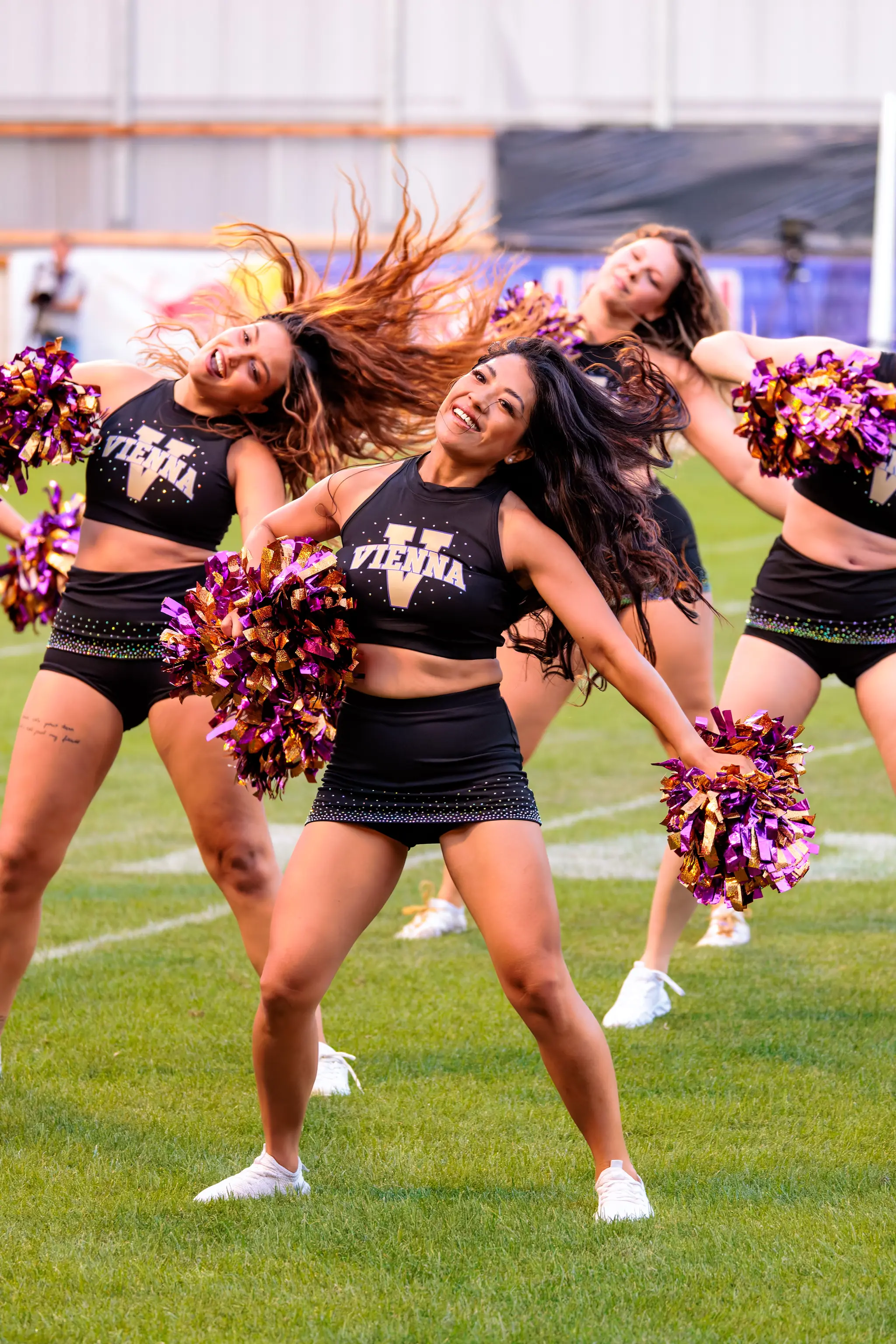 Drei Cheerleaderinnen des Spirit Squad führen eine Choreografie mit violett-goldenen Pompons auf.