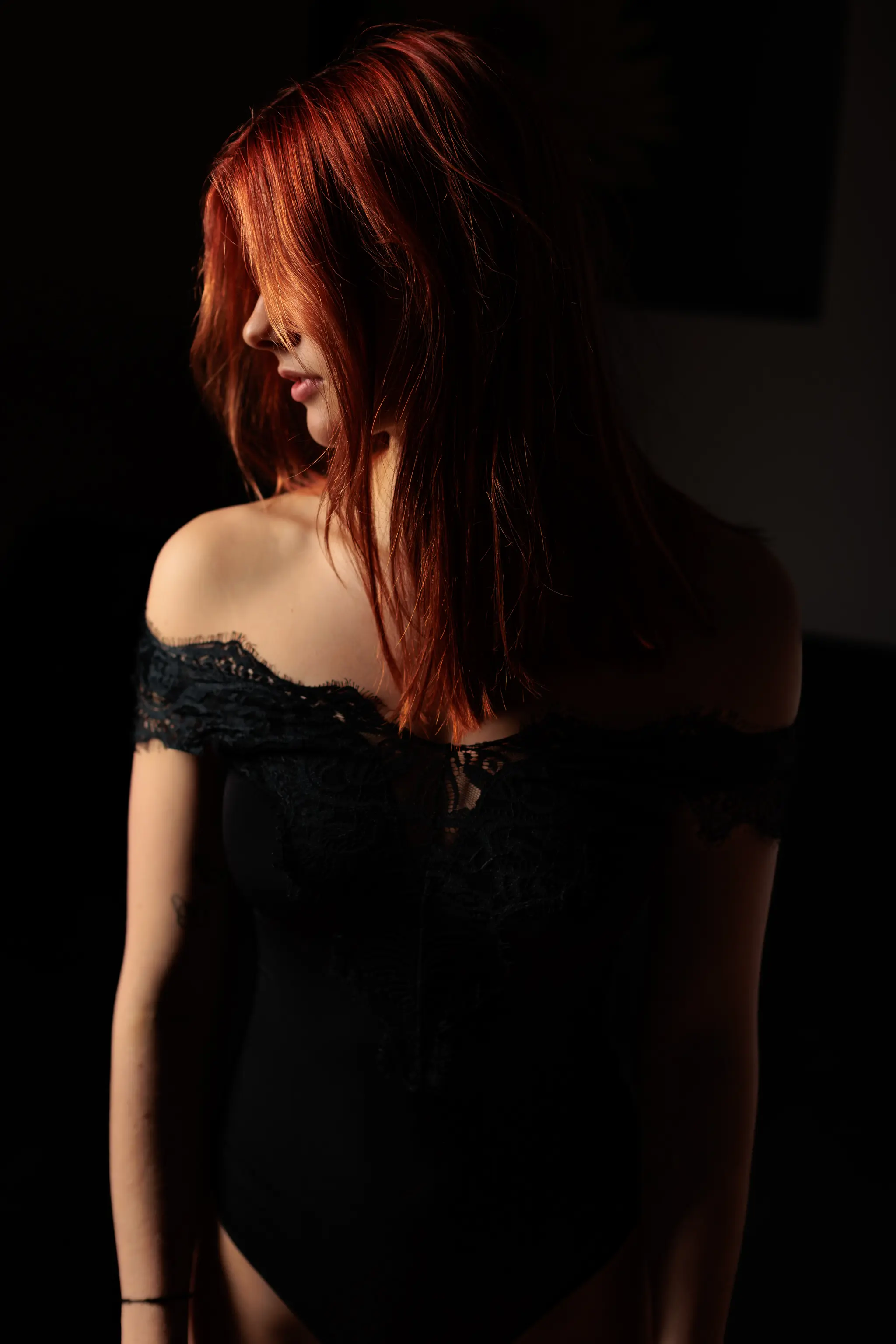 Geheimnisvolles Profil-Portrait von Sarah mit leuchtend roten Haaren in einem eleganten schwarzen Spitzen-Body bei stimmungsvoller Lichtsetzung