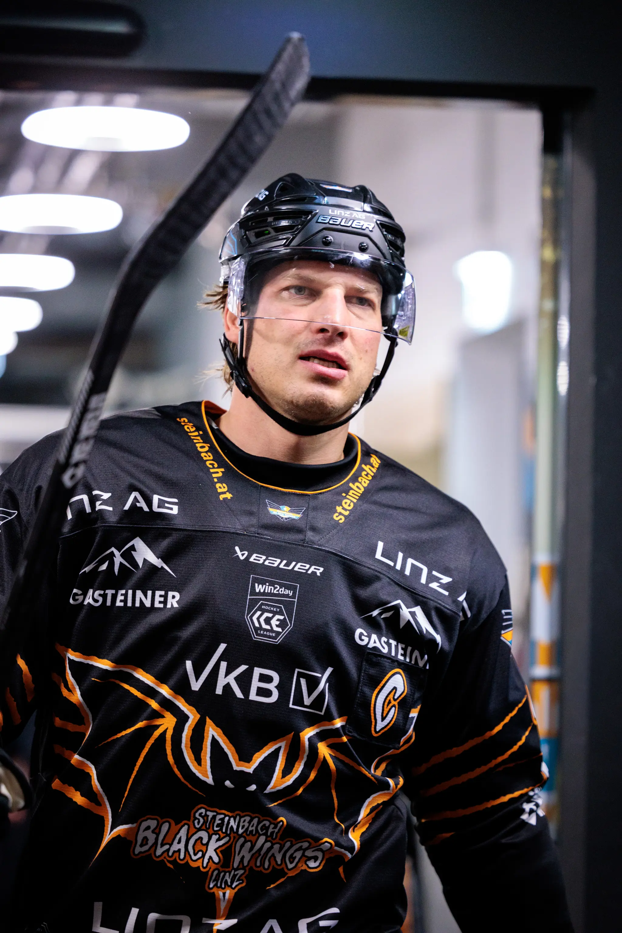 Nahaufnahme eines konzentrierten Eishockeyspielers der Steinbach Black Wings Linz in seinem schwarzen Trikot mit Helm und Schläger