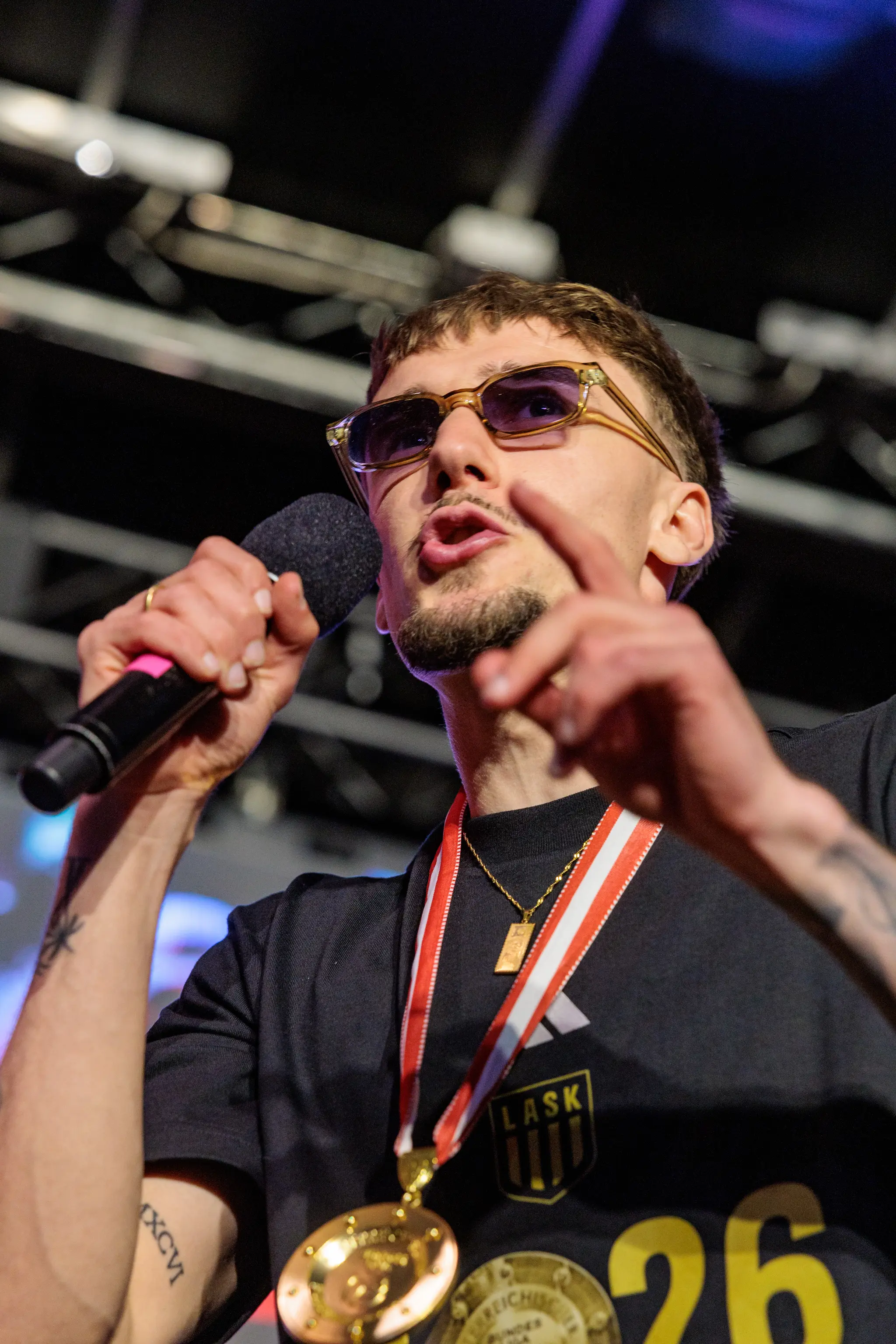 Ein LASK-Spieler mit Sonnenbrille spricht mit einem Mikrofon und zeigt mit dem Finger während der Meisterfeier auf der Bühne