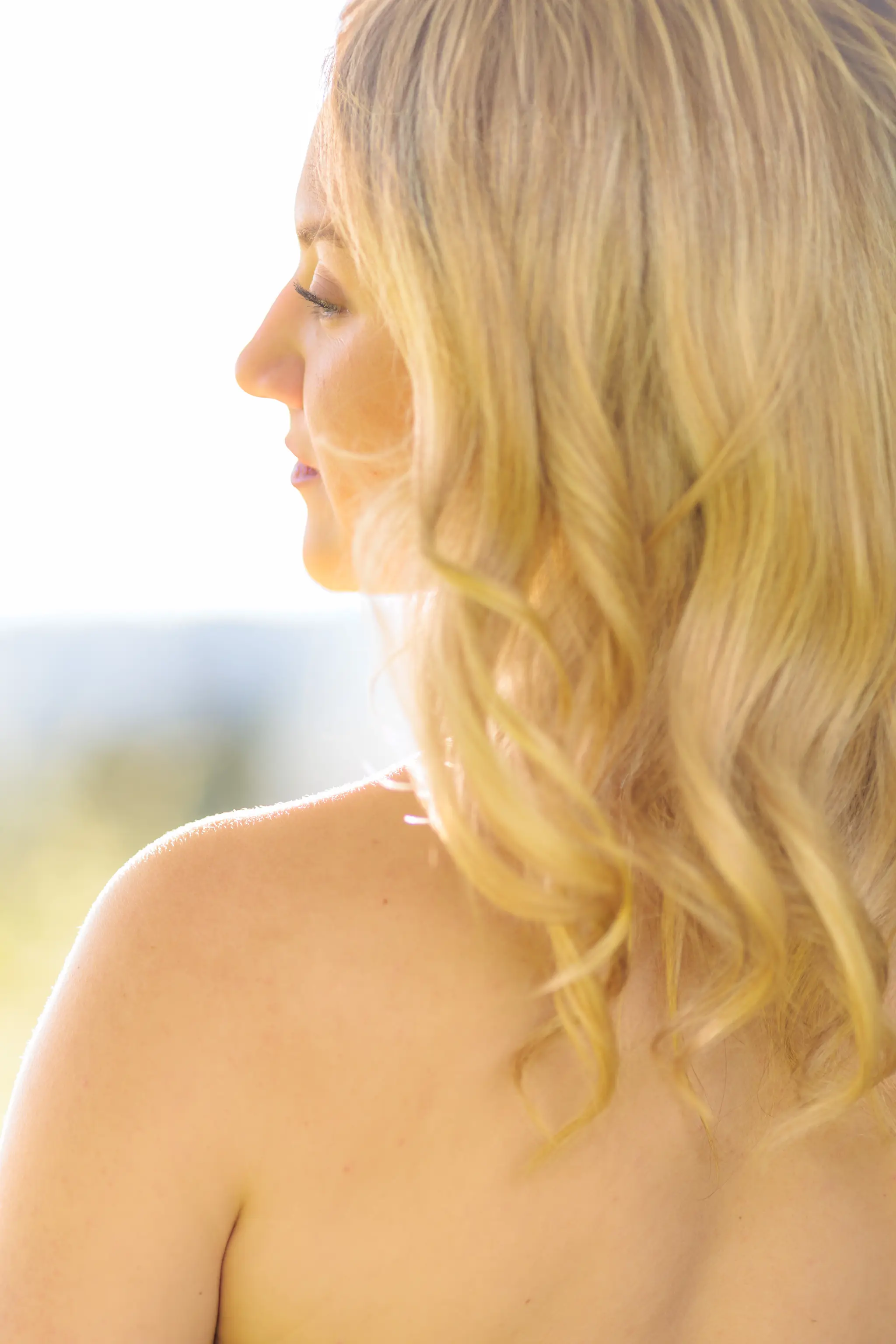 Eine blonde Frau ist im Profil zu sehen, ihr gewelltes Haar und ihre Schulter werden von warmem Gegenlicht sanft beleuchtet 