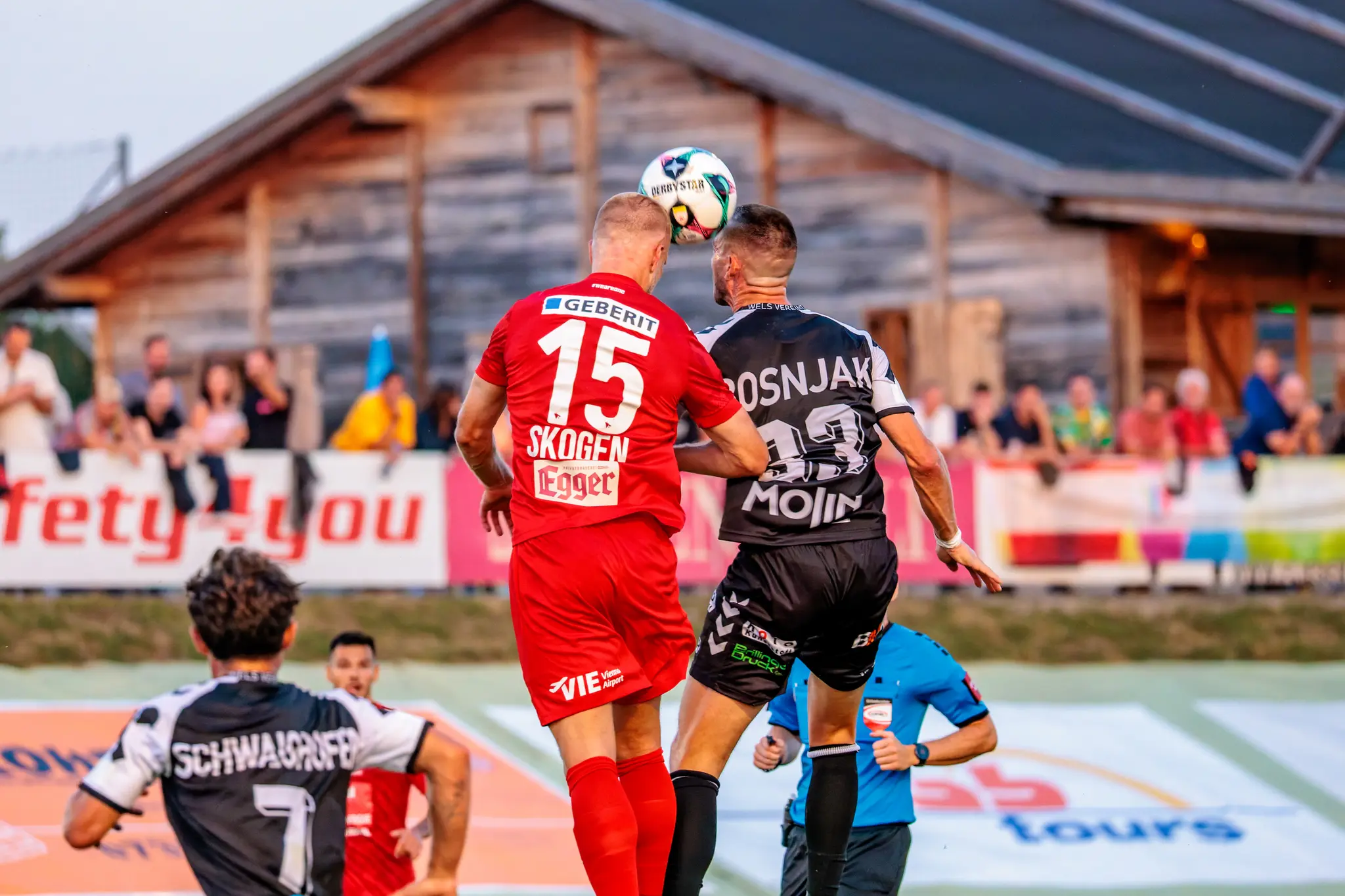 Ein Spieler von SPG HOGO Wels im roten Trikot und ein Spieler von SKN St. Pölten im schwarz-weißen Trikot liefern sich ein intensives Kopfballduell im ÖFB-Cup