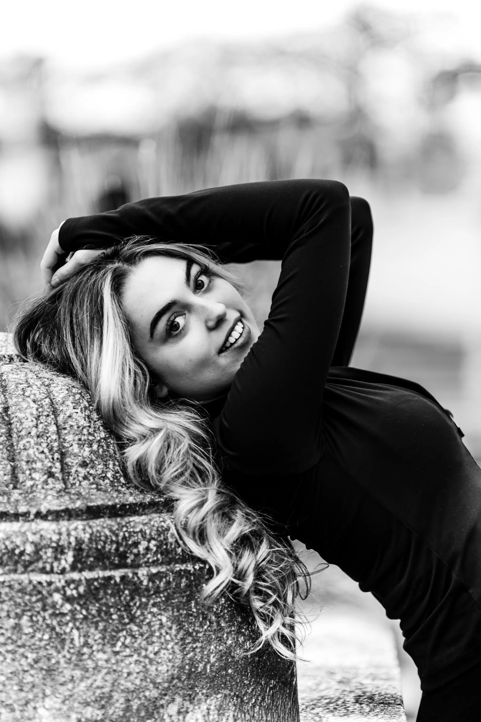 Schwarz-Weiß-Porträt von Model Valentina, die sich im Wiener Stadtpark an einen Stein lehnt, ihre Hände hinter dem Kopf verschränkt hat und direkt in die Kamera blickt