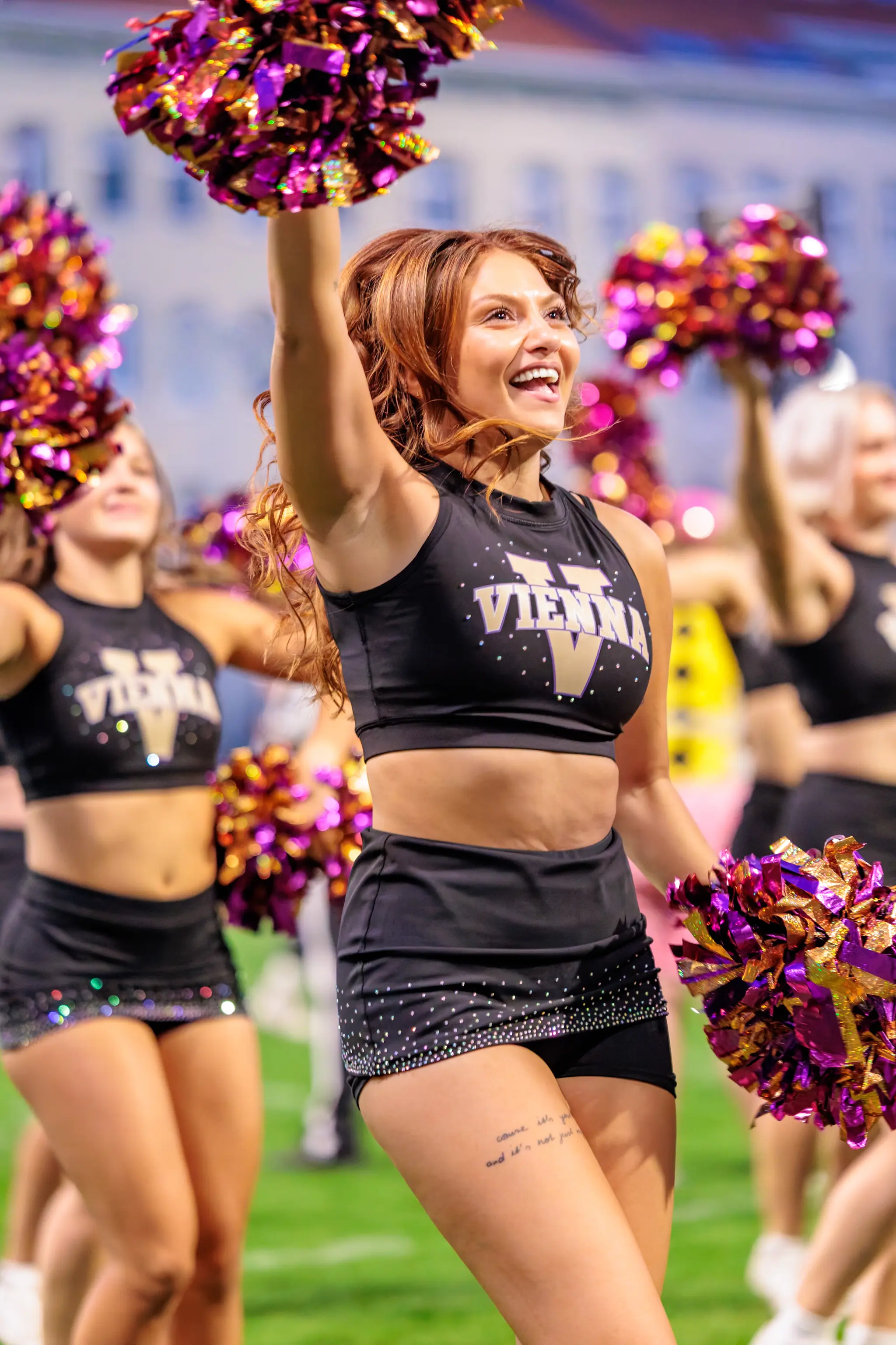 Im Abendlicht reckt eine Tänzerin des Vienna Vikings Cheer Squads ihren lila-goldenen Pompon in die Höhe und lacht – Showeinlage in der Pause des dritten Viertels.
