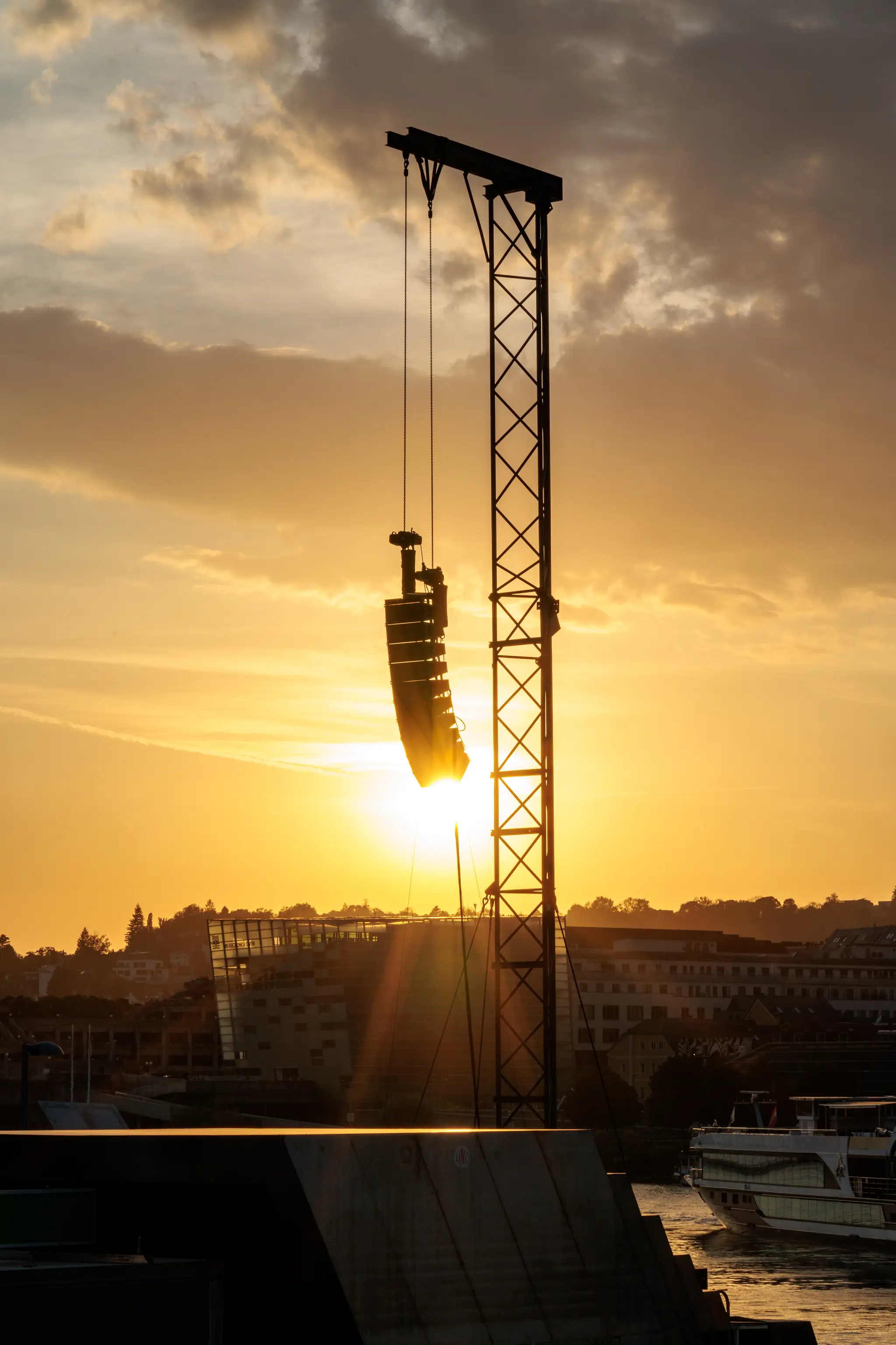 Dramatischer Sonnenuntergang mit silhouettierter PA-Anlage, die an einem Rigging-Turm über der Donau in Linz hängt 