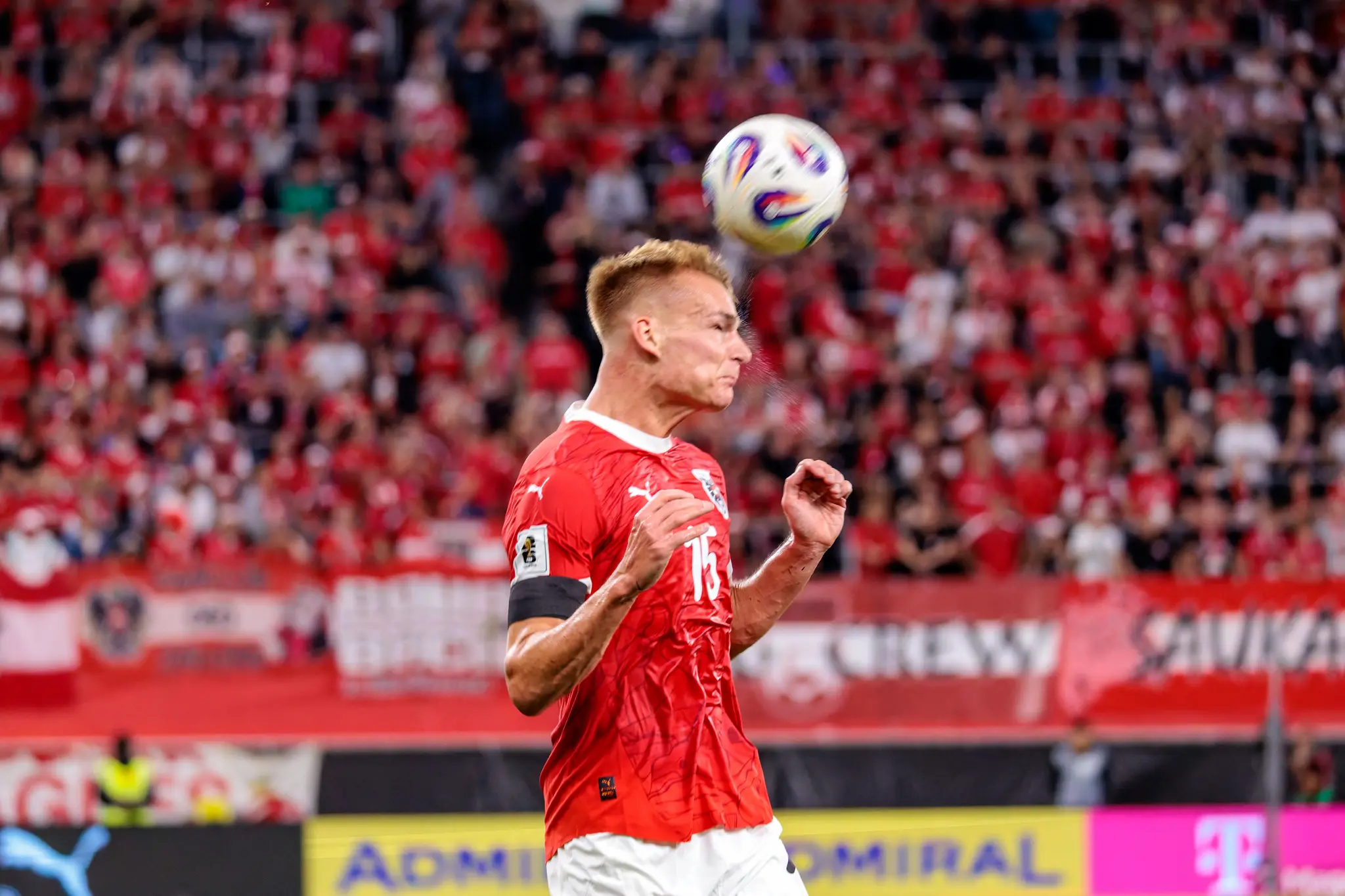 Philipp Lienhart, ein österreichischer Fußballspieler im roten Trikot mit der Nummer 15, köpft den Ball während eines Fußballspiels gegen Zypern vor einer unscharfen Zuschauerkulisse
