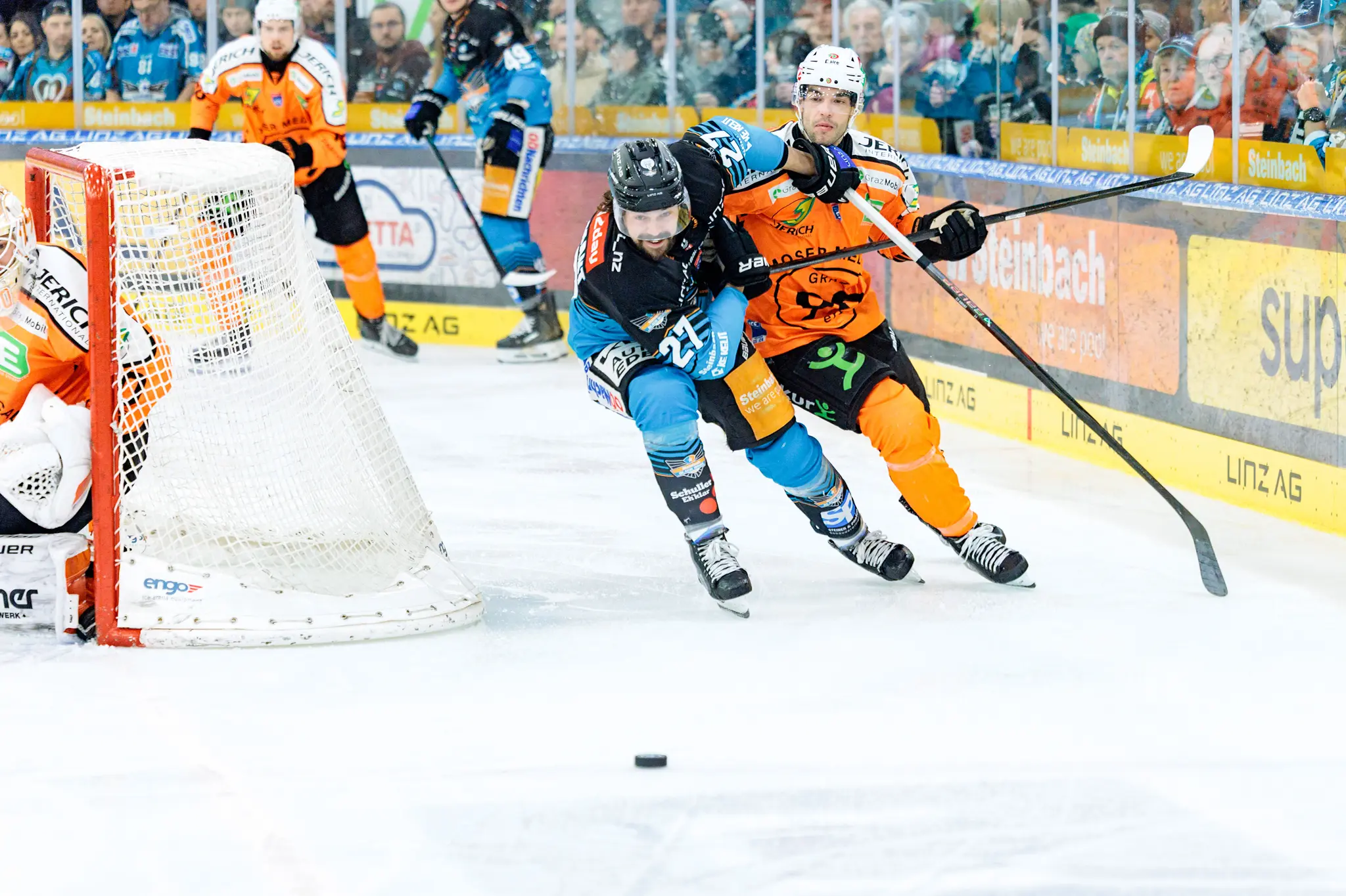 Ein intensiver Eishockey-Zweikampf um den Puck zwischen Shawn St. Amant und einem grazer Spieler direkt vor dem Tor, mit dem Torwart in seiner Position